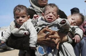 img_20240330_200524_5608168648864783349633-300x197 A woman carries three babies as she reaches the central part of the Gaza Strip after fleeing the Al-Shifa hospital compound in Gaza City, on March 21, 2024.